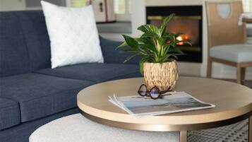 Un salon avec un canapé, une table basse ronde sur laquelle se trouvent un magazine et des verres, et une plante dans un pot en fibres tressées.