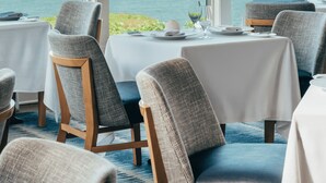 A dining area with tables set for two, overlooking a body of water with a sailboat. - Wequassett Resort and Golf Club (Harwich)