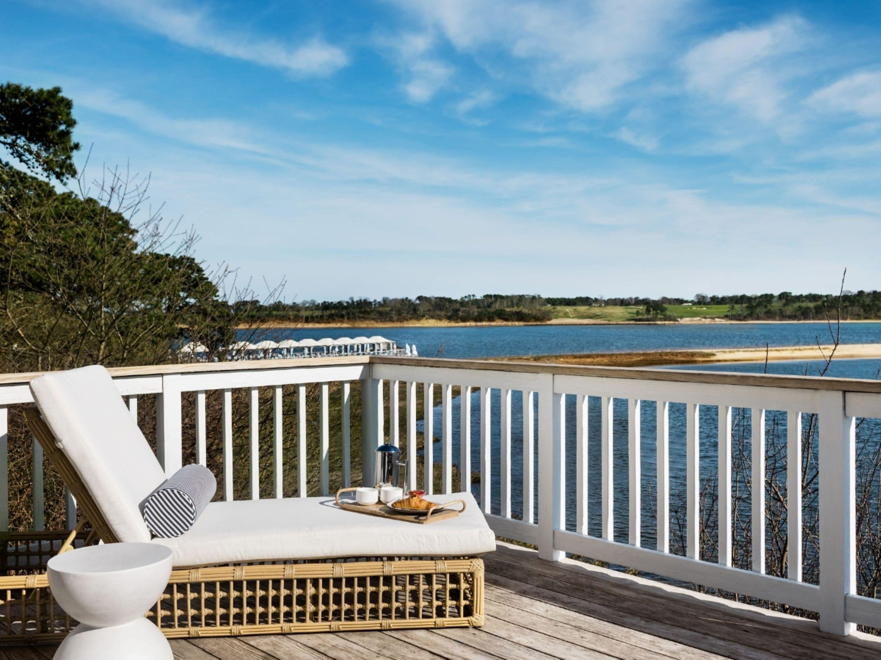 A deck with a white railing, a wicker lounge chair, and a table with a tray of items.