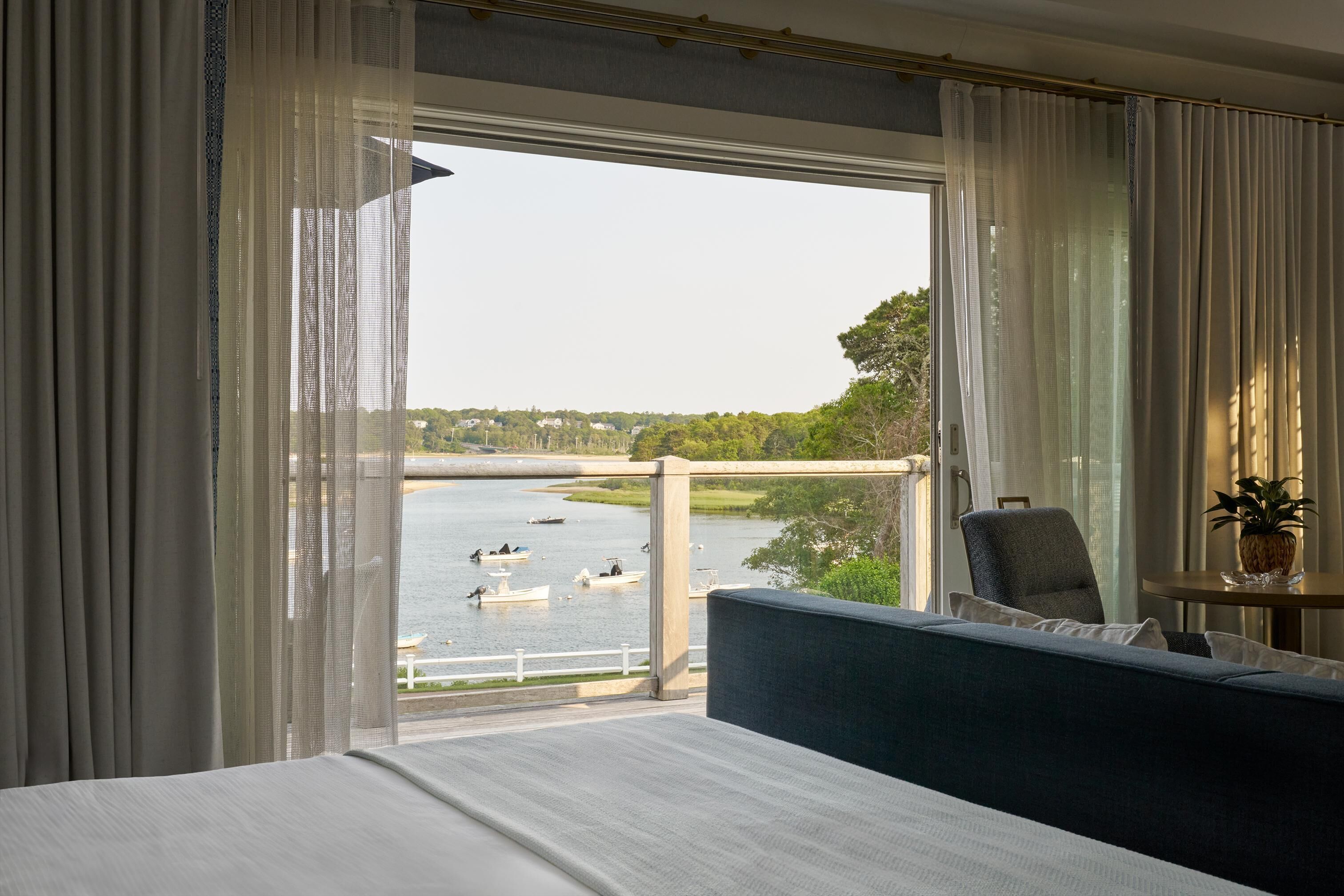 Ein Hotelzimmer mit einem großen Bett, Seeblick mit Booten und einem Balkon mit Stuhl und Pflanze.