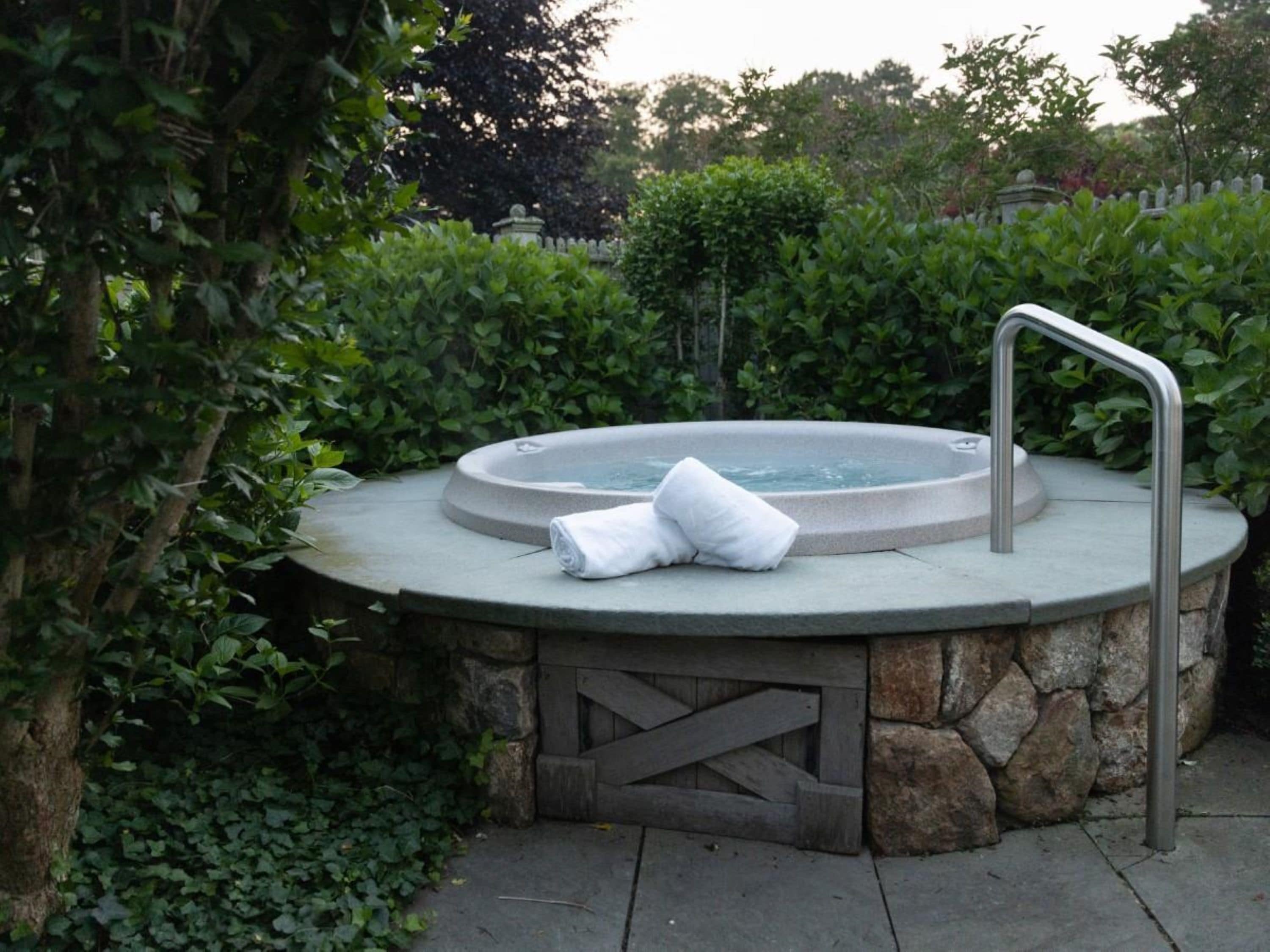 A hot tub with a stone wall, a wooden gate, and lush greenery.