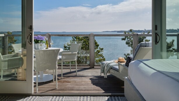 A balcony with wicker furniture, a table with a vase and wine glass, and a view of the sea. - Wequassett Resort and Golf Club (Harwich)