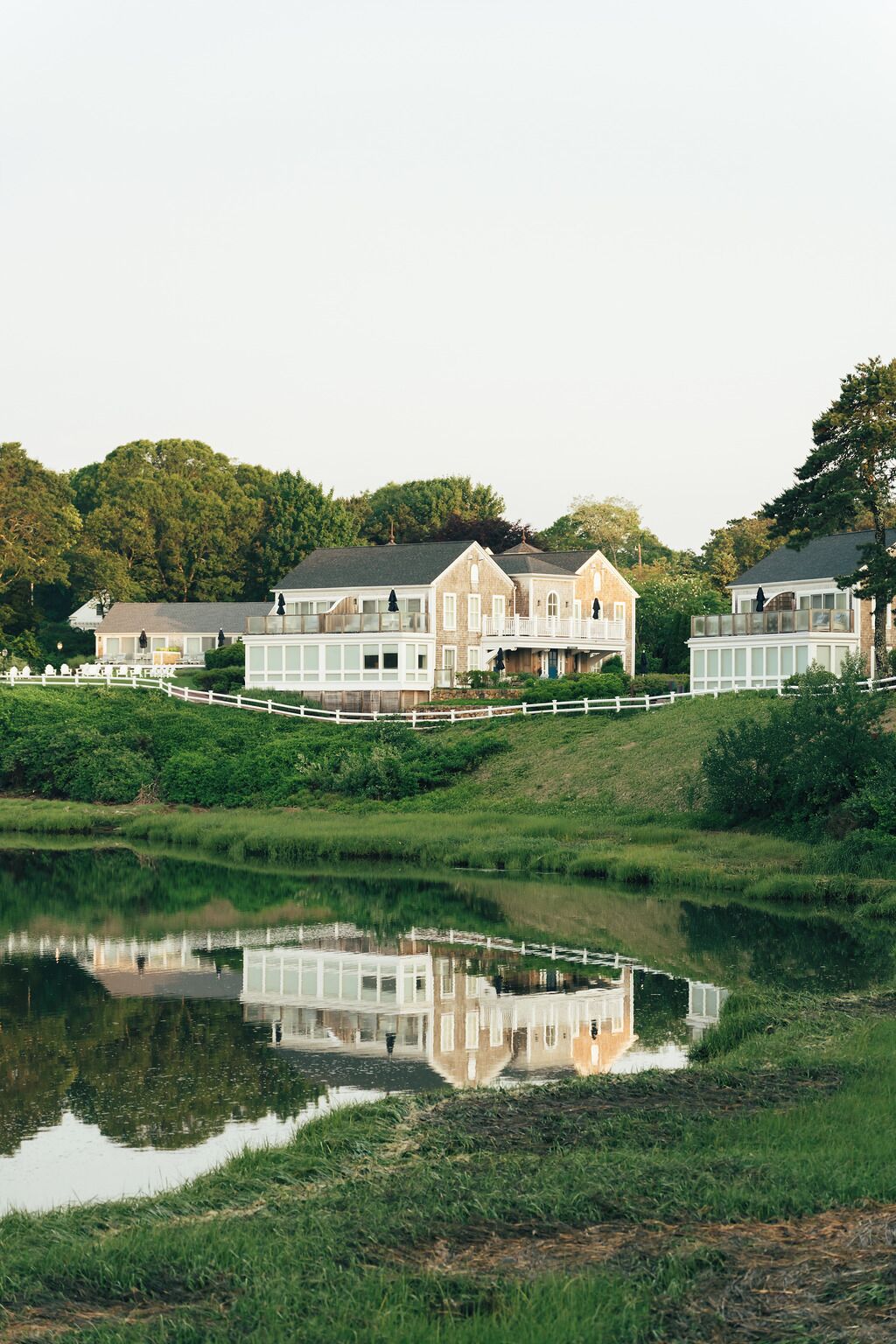 A large, multi-story house with a reflective pond in front.