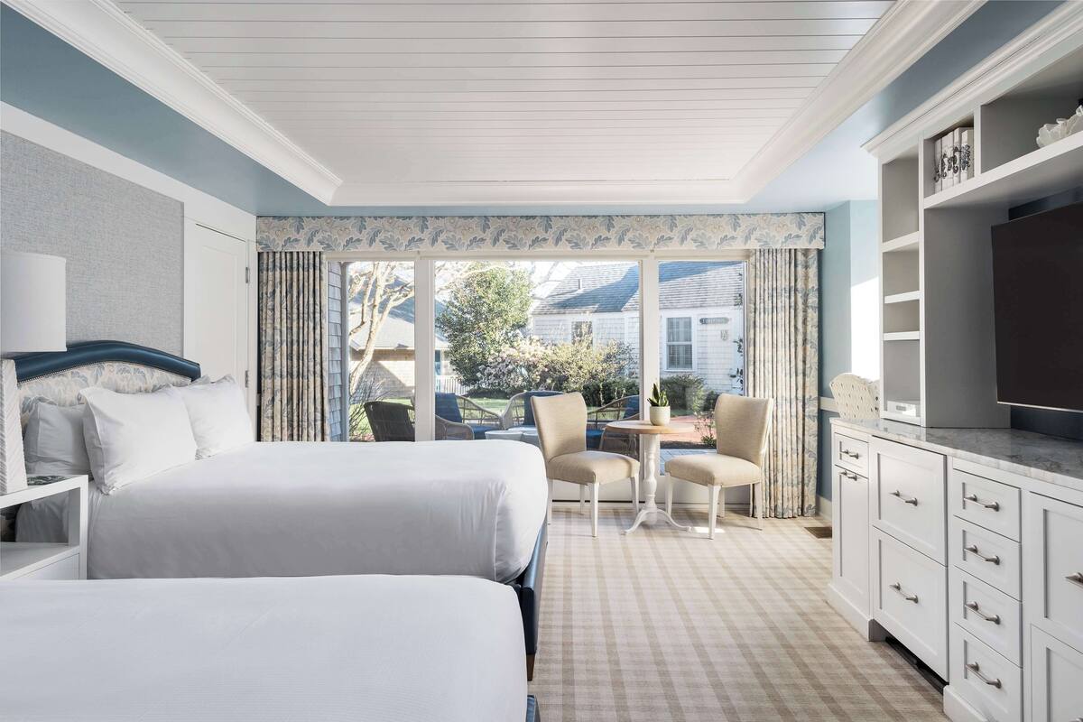 A hotel room with two beds, a dining area with a table and chairs, and a TV on a cabinet.