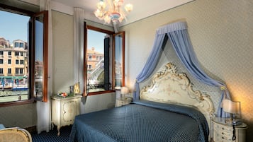 Quarto com cama grande, mesa de cabeceira, cômoda, lustre e janela com vista para prédios.