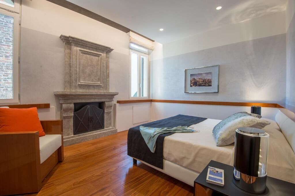 A hotel room with a bed, a fireplace, a window, and a framed picture on the wall.