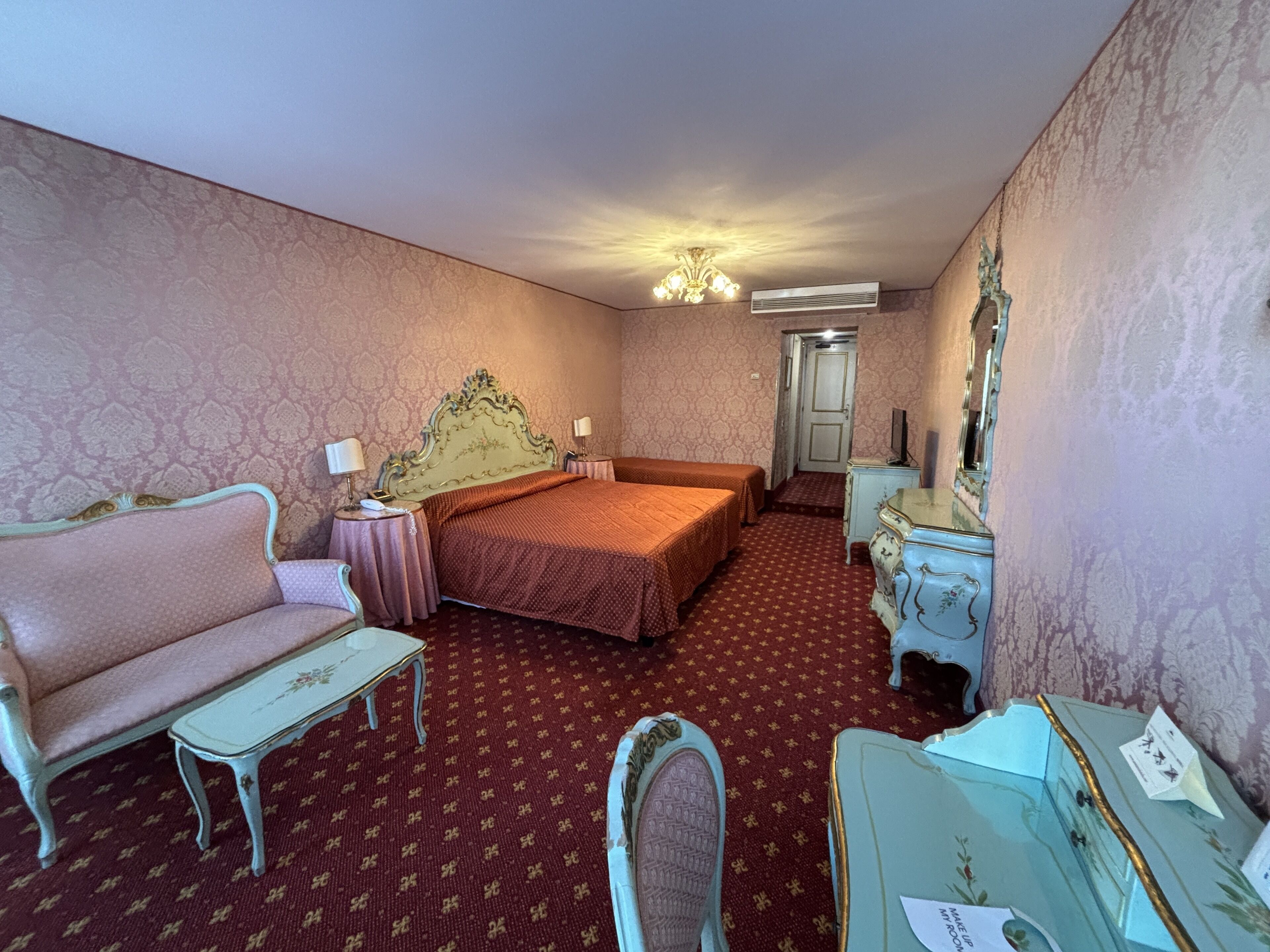 A hotel room with a bed, a sofa, a small table, a dresser, and a mirror.