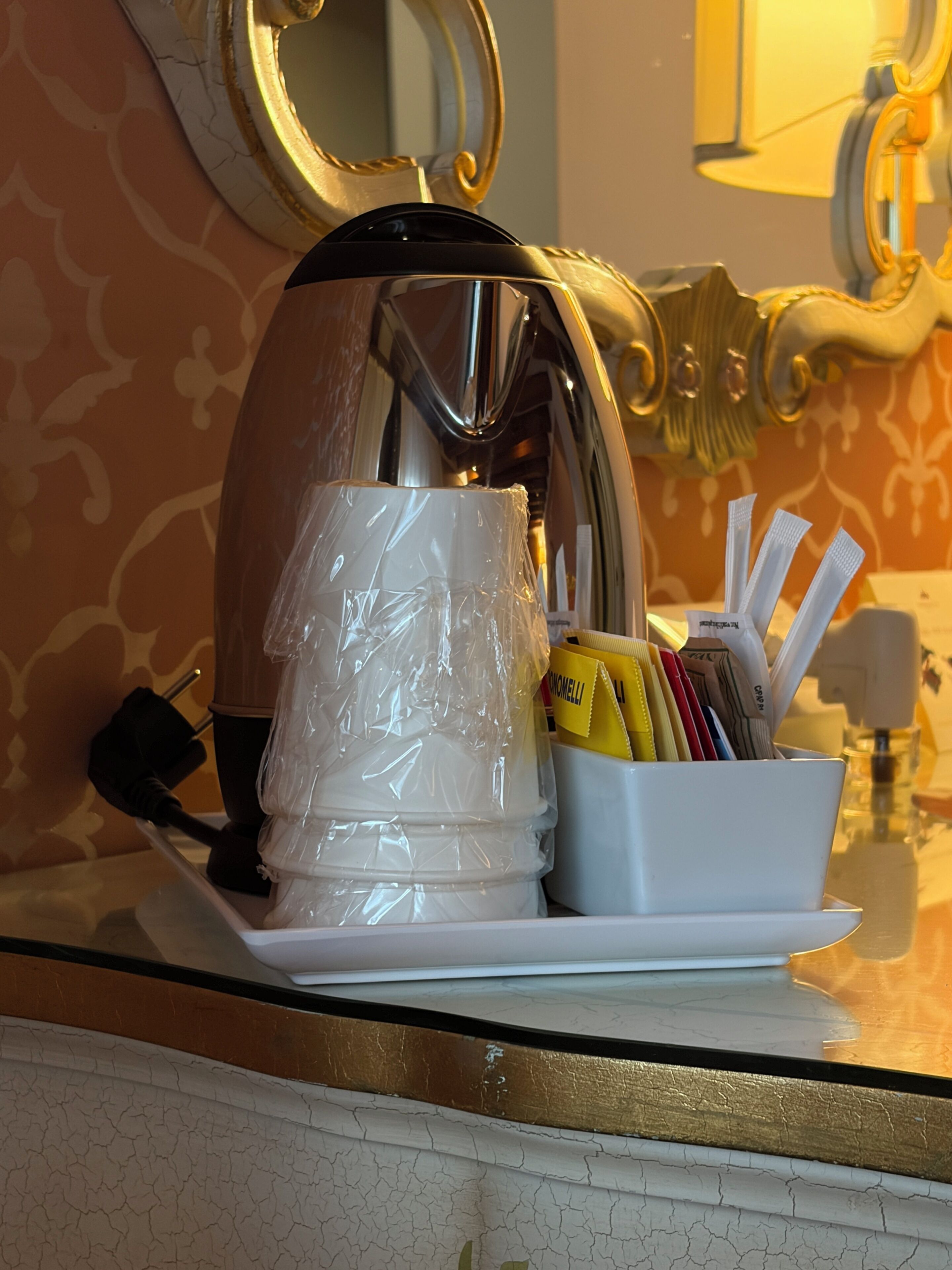 A kitchen area with a coffee maker, a white cup, and a container holding utensils and condiments.