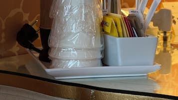 Un área de cocina con cafetera, taza blanca y un recipiente con utensilios y condimentos.