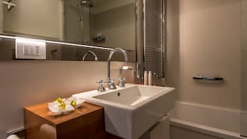 Un baño moderno con un lavamanos blanco, dos grifos, un espejo y una cabina de ducha con mampara de vidrio.