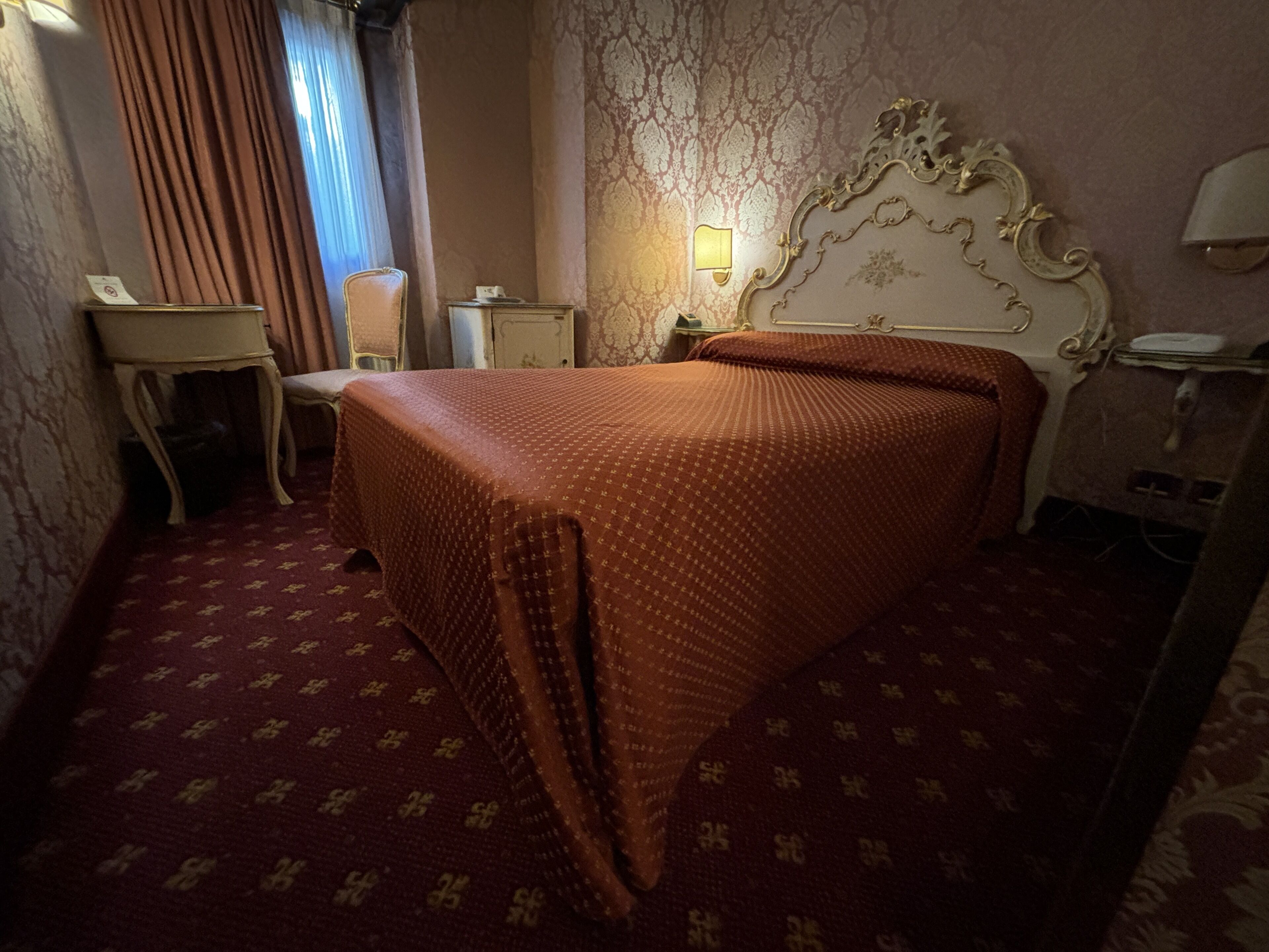 Una habitación de hotel con cama, mesita de noche, silla, una pequeña mesa y espejo.