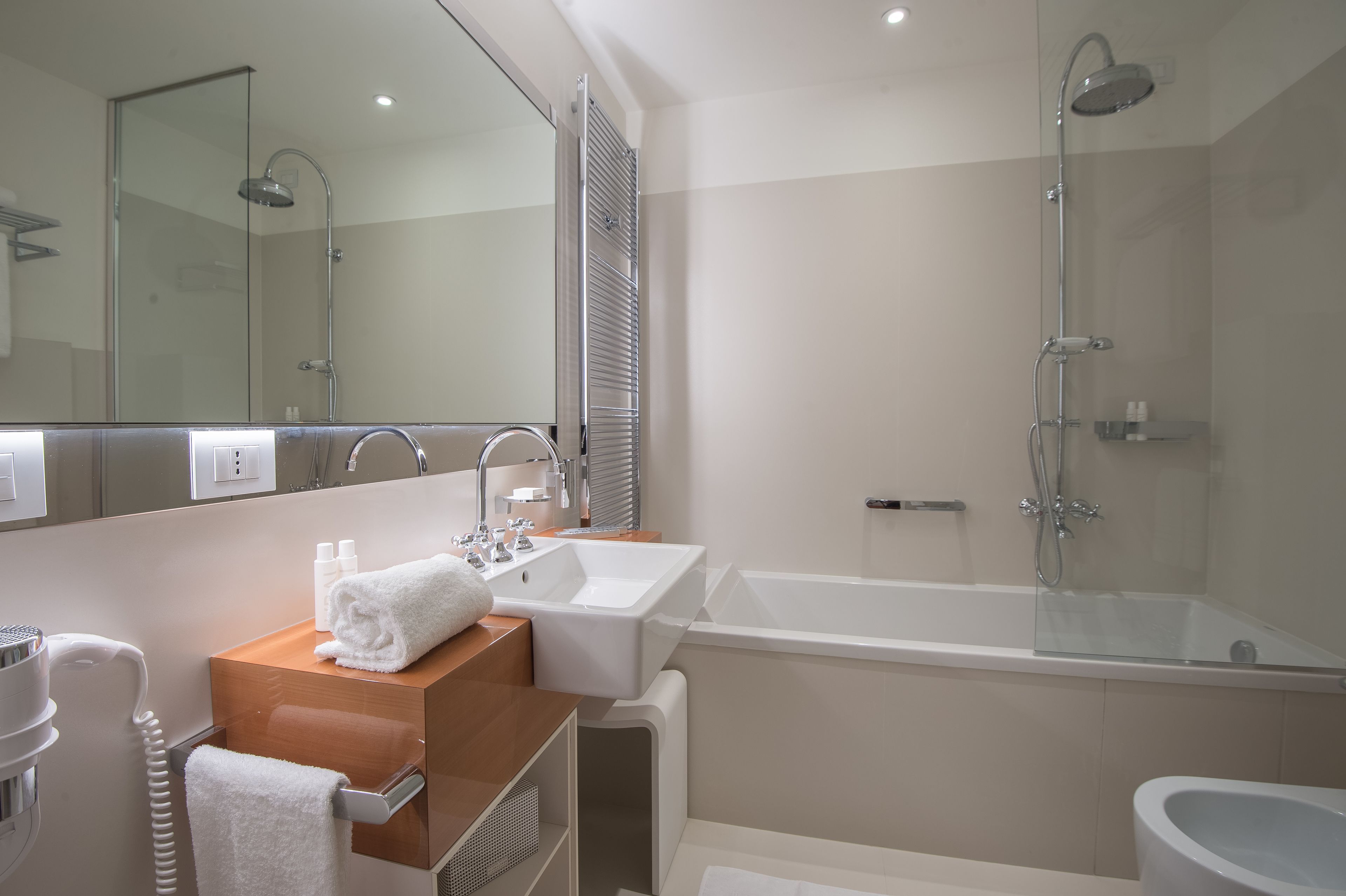 Un baño moderno con ducha de vidrio, un lavamanos blanco y un espejo sobre el mueble.