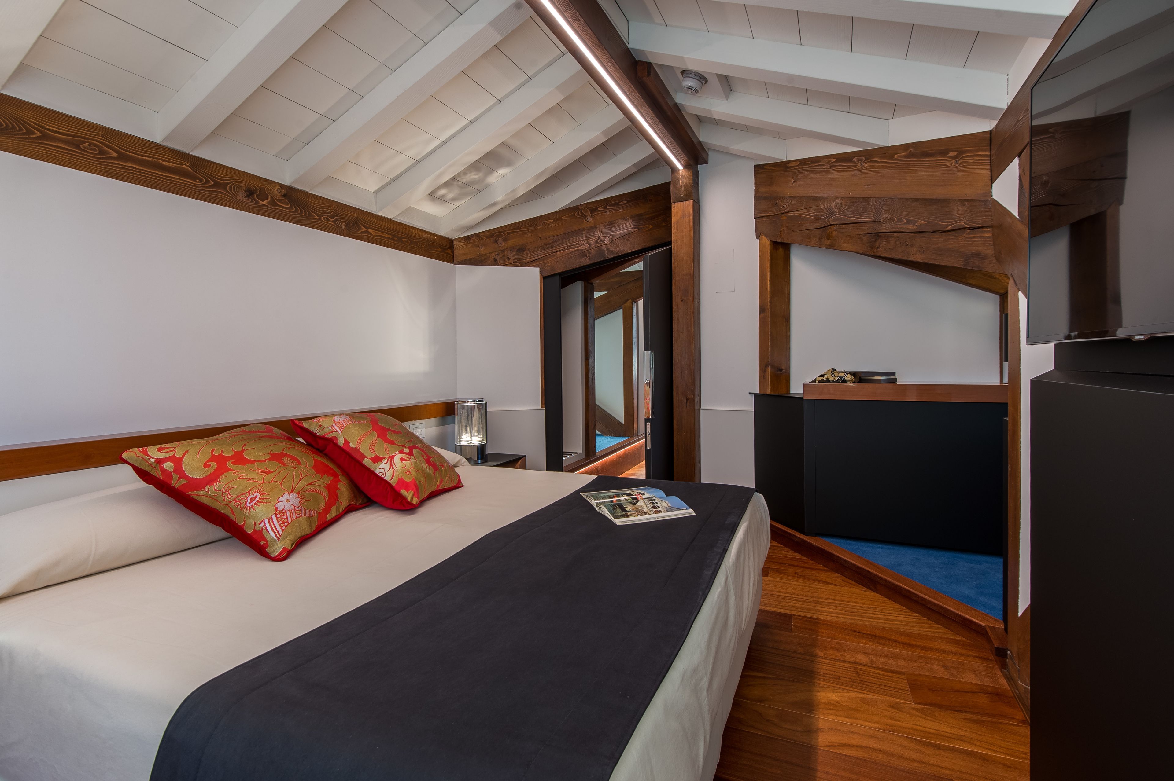 Camera d'albergo con un letto, travi in legno, una TV e un tavolino.