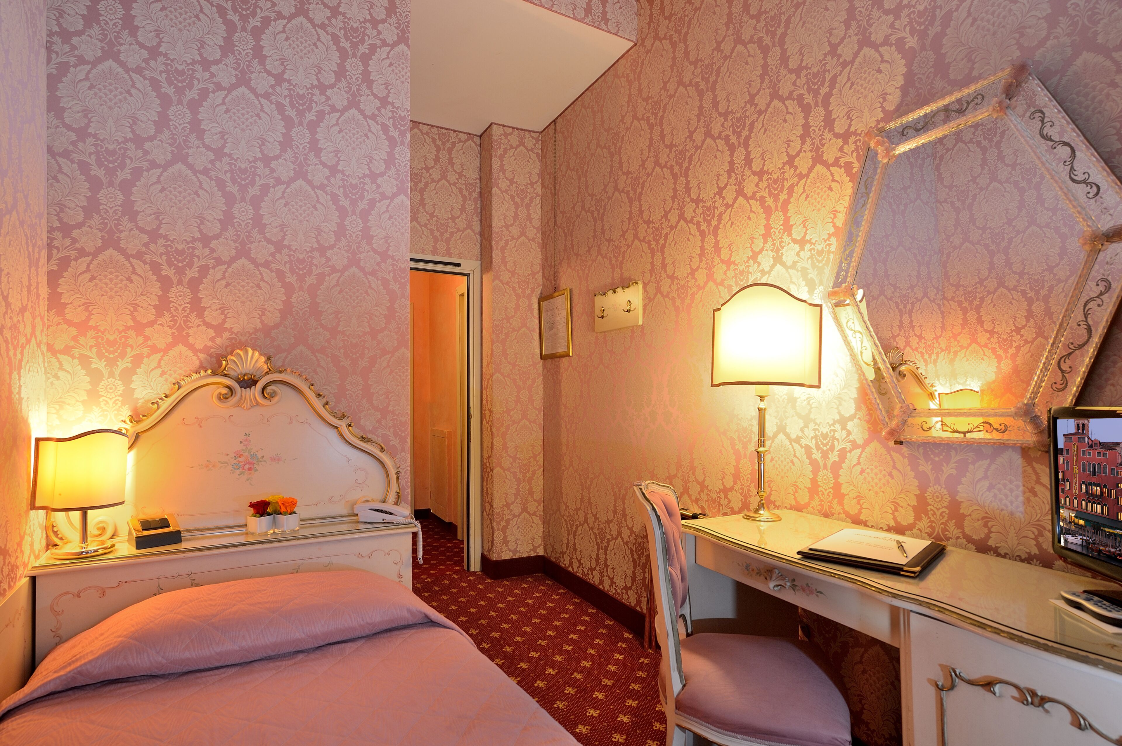 A hotel room with a bed, desk, chair, and a mirror.