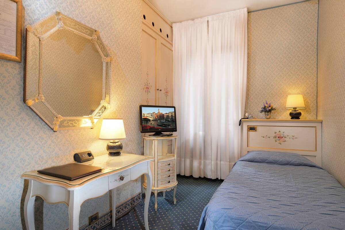 A hotel room with a bed, a desk with a lamp, a television, and a mirror.