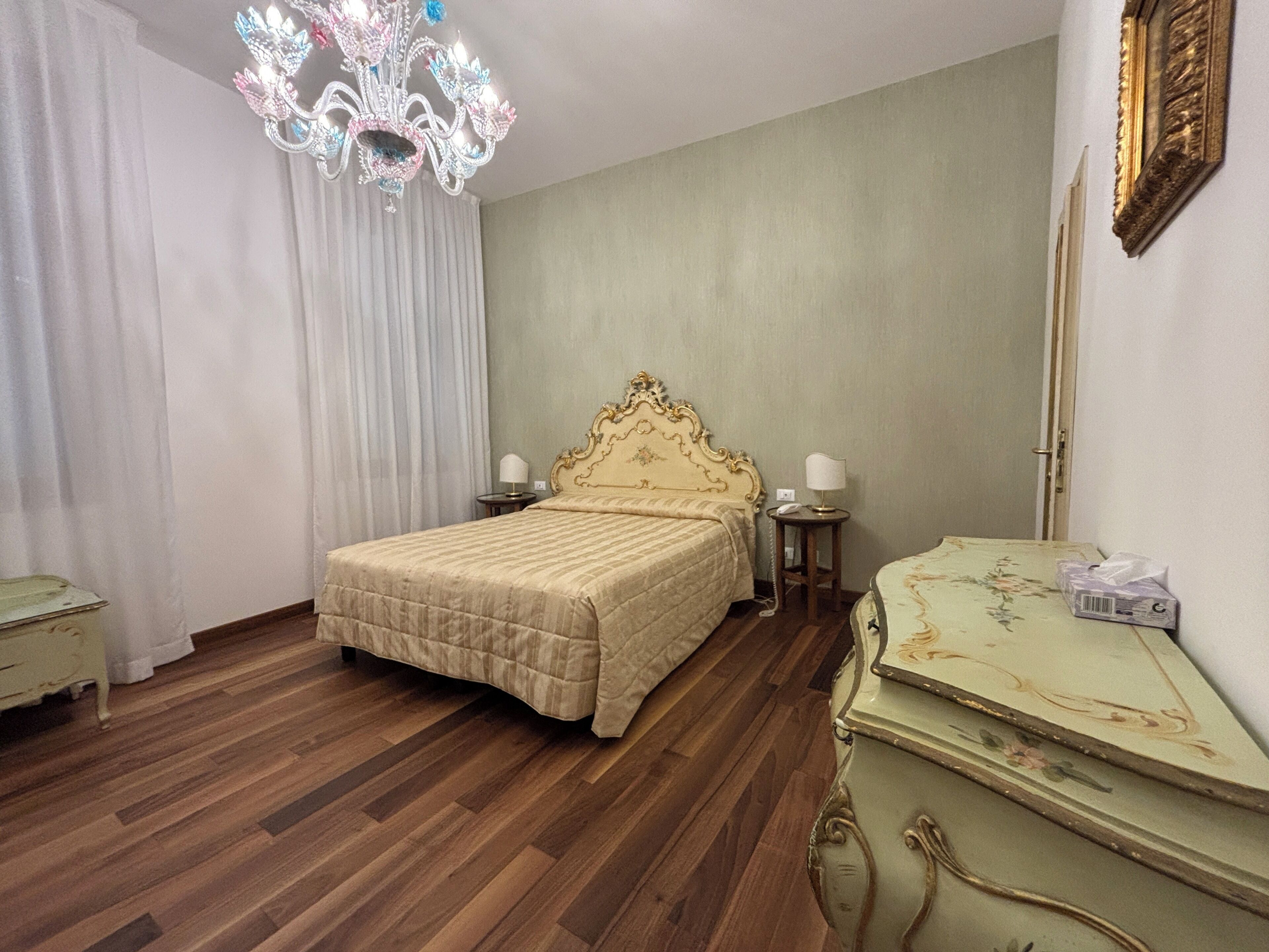 A hotel room with a large bed, a chandelier, a dresser, and a mirror.
