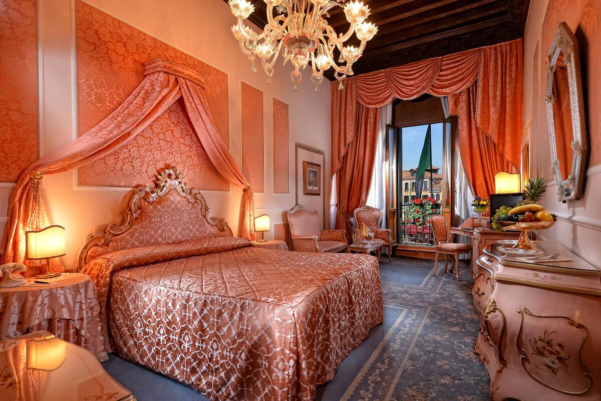 A luxurious bedroom with a large bed, ornate chandelier, and classic decor.