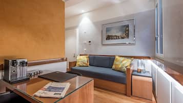 Ein modernes Hotelzimmer mit einer Couch, einem Glastisch, einer Kaffeemaschine und einem Bild an der Wand.