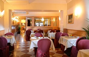 A restaurant with checkered flooring, tables with white tablecloths, and chairs with red upholstery.