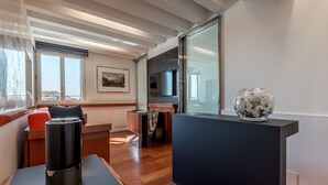 A modern living room with a wooden floor, a sofa, a coffee table, and a TV mounted on the wall. - Hotel Rialto (Venice)