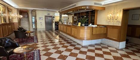 Un hall de hotel con piso a cuadros, un mostrador de recepción y zonas de estar.