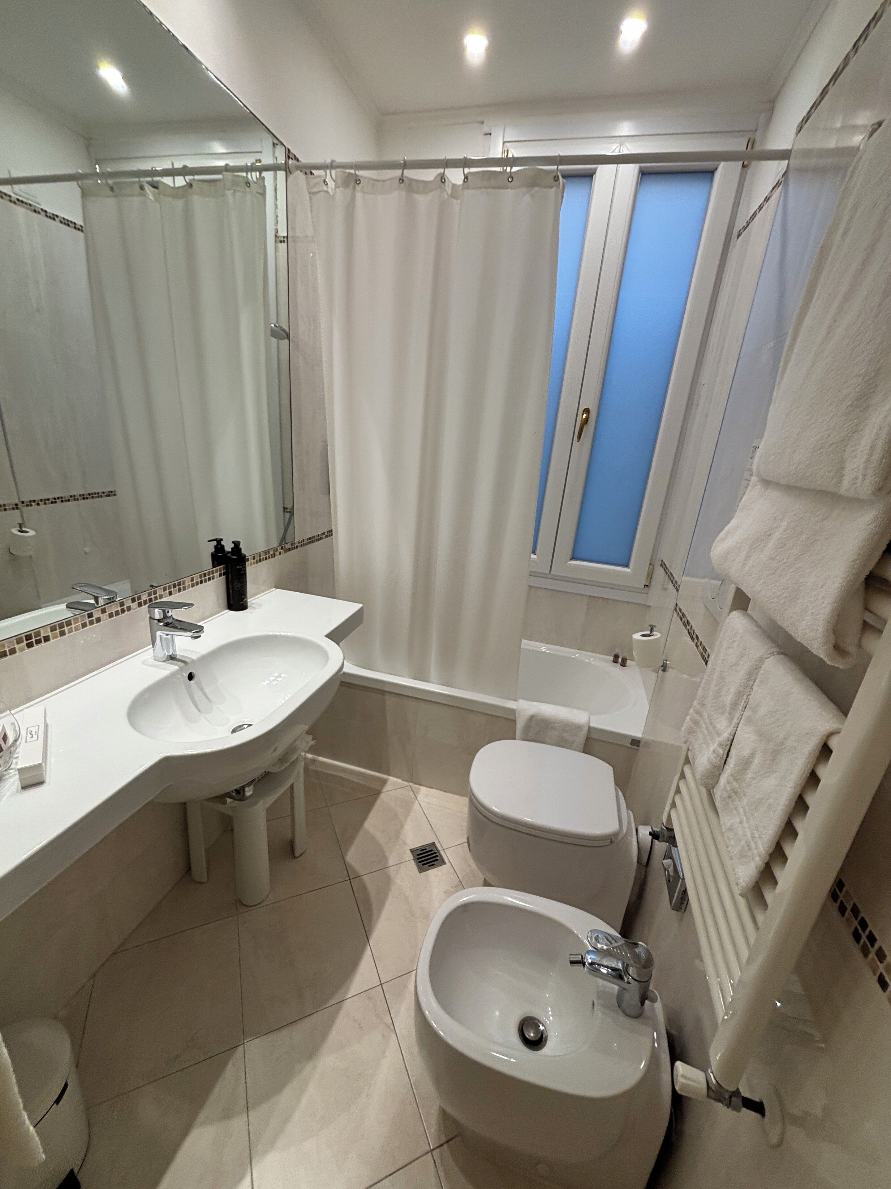 Un baño moderno con un espejo grande, un lavabo, un bidé y una zona de ducha.