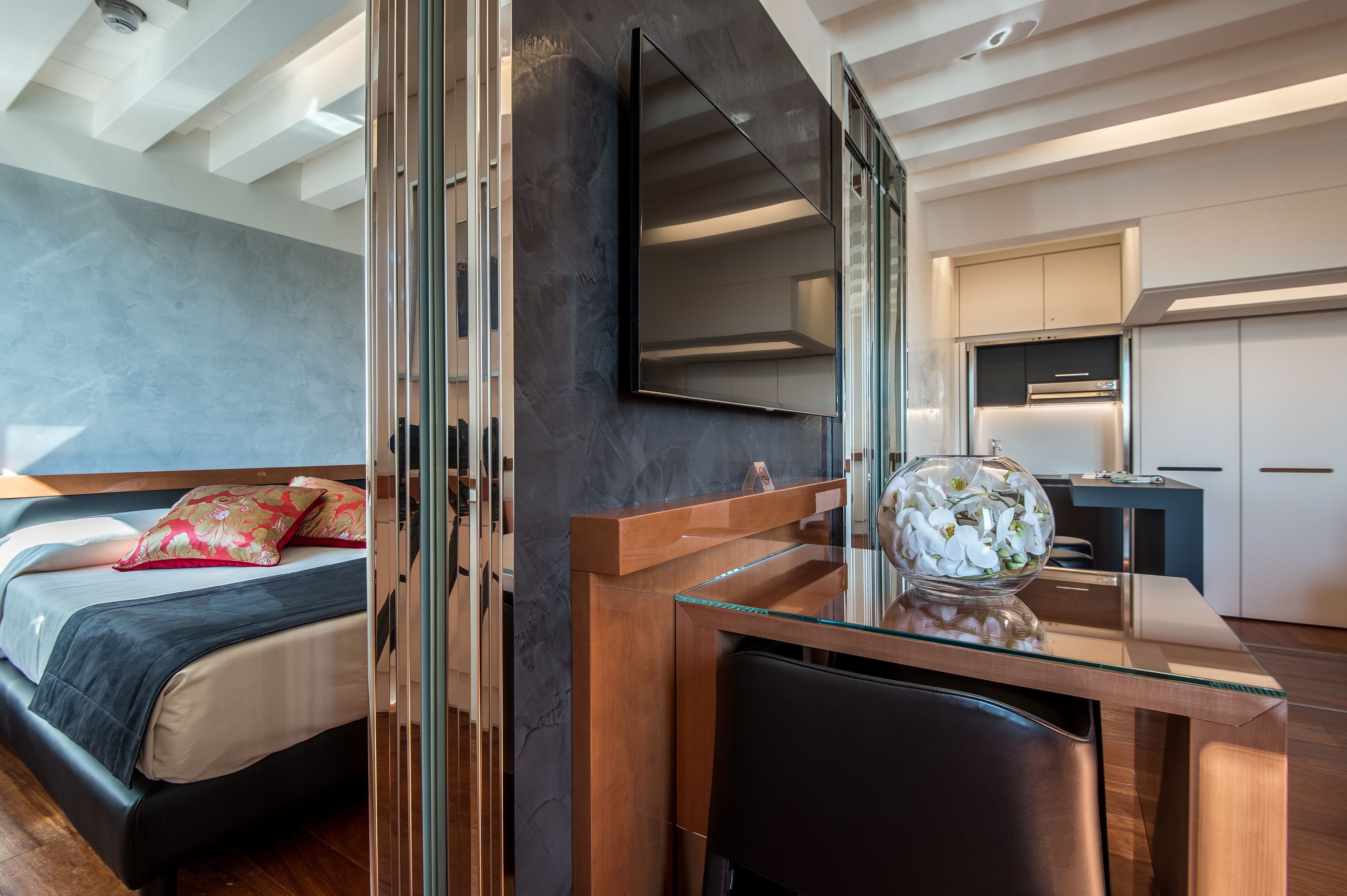Una habitación de hotel moderna con cama, escritorio de cristal, espejo y zona de cocina.