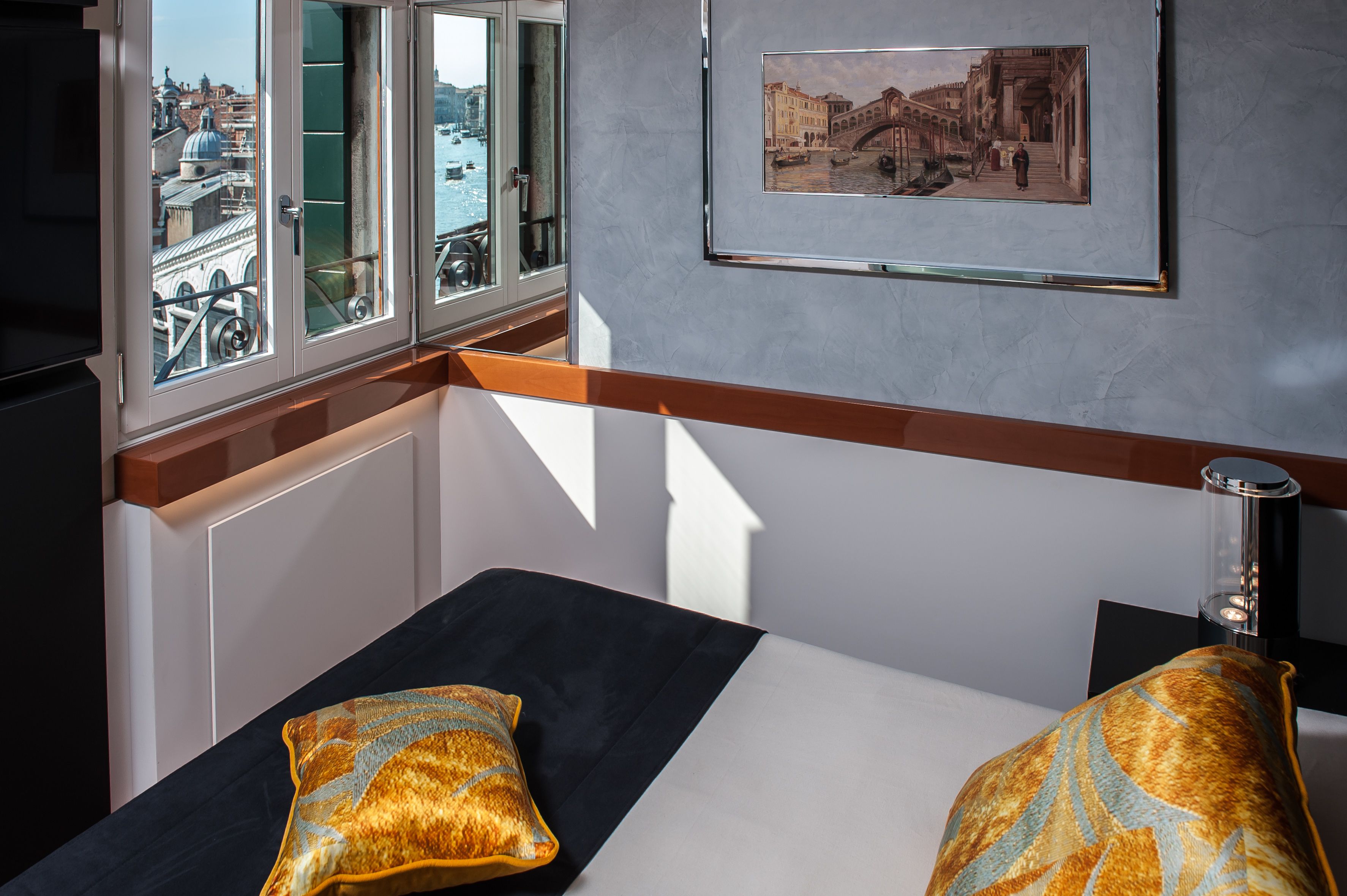 Habitación de hotel con cama, dos almohadas, un cuadro en la pared y ventana con vista a edificios y agua.