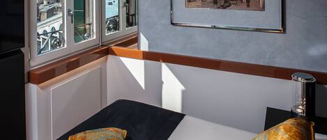 Habitación de hotel con cama, dos almohadas, un cuadro en la pared y ventana con vista a edificios y agua.