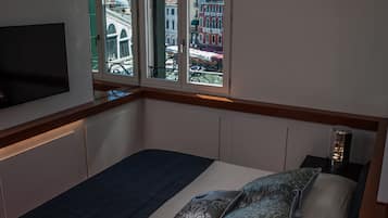 A bedroom with a bed, a TV mounted on the wall, and a view of a cityscape through a window.