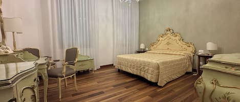 Una habitación de hotel con piso de madera, una cama con cabecera dorada, un escritorio con silla y un candelabro.