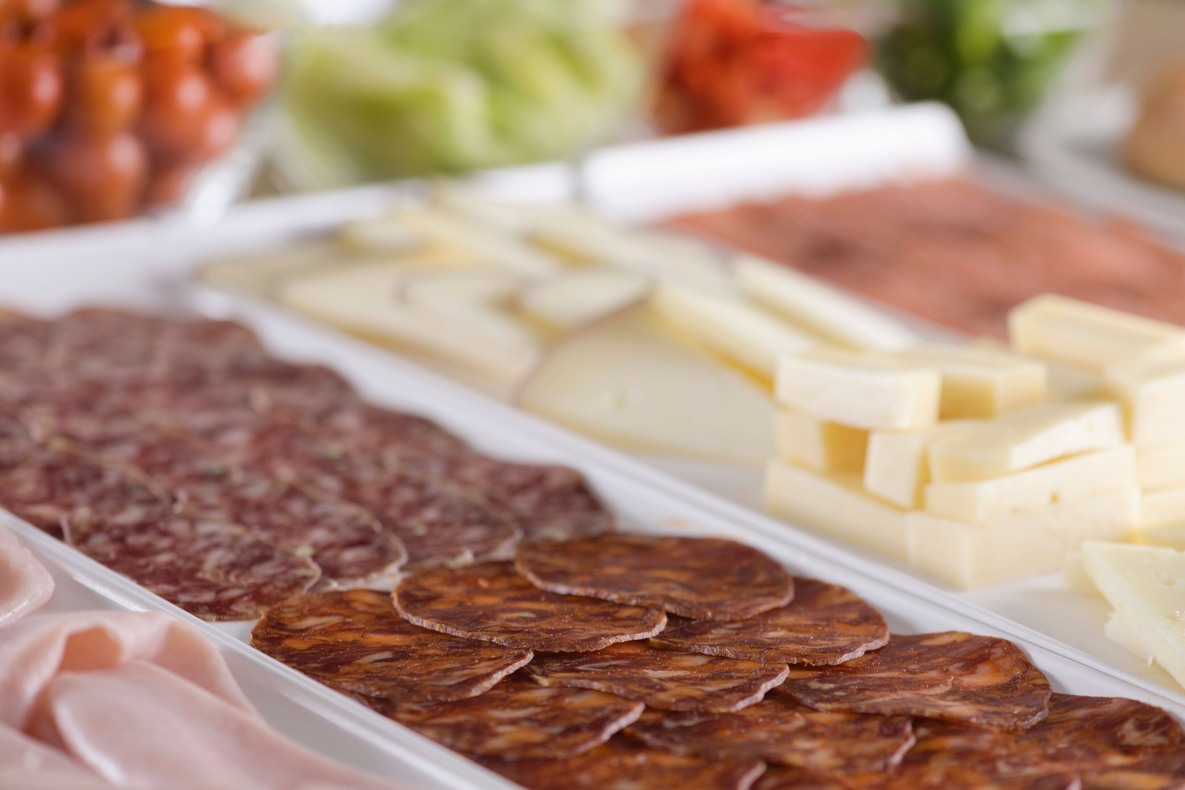 Variedad de alimentos, incluyendo fiambres y quesos, en una bandeja.