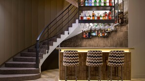 Een bar met een wenteltrap, een houten toog en drie barstoelen.