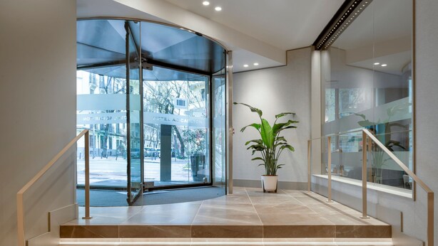 Een moderne hotellobby met een glazen entree, een potplant en een trap naar de verdiepingen erboven.