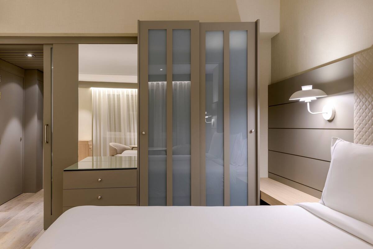 Ein Schlafzimmer mit einem Bett, einem Nachttisch, einer Kommode und einer Schiebetür mit Milchglasfenstern.