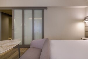 Ein modernes Hotelzimmer mit einer Schiebeglastür, einem kleinen Tisch, einer Couch und einer Nachttischlampe.