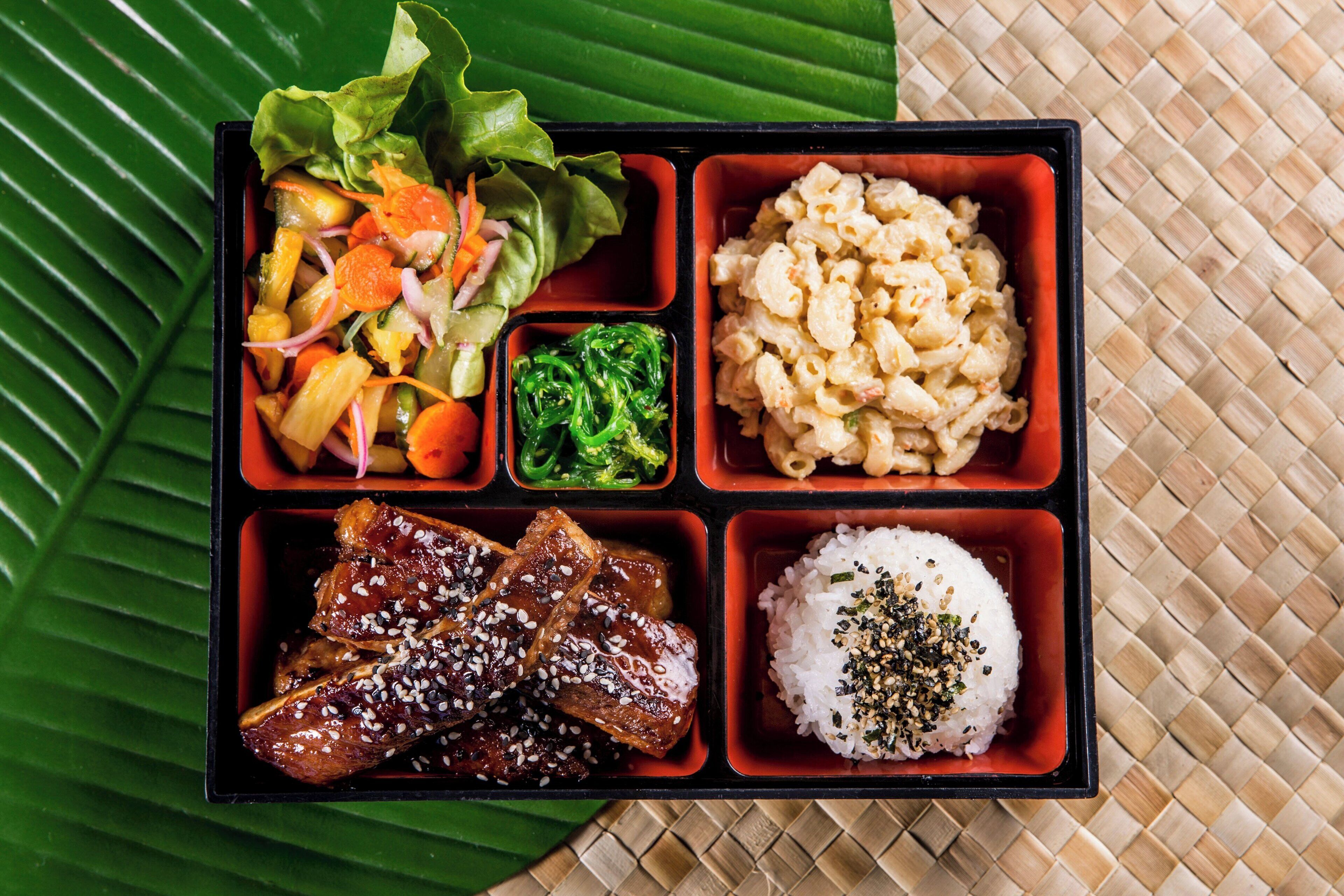 En bento-boks med forskellige spiser, herunder ris, kød, grøntsager og makaroni.