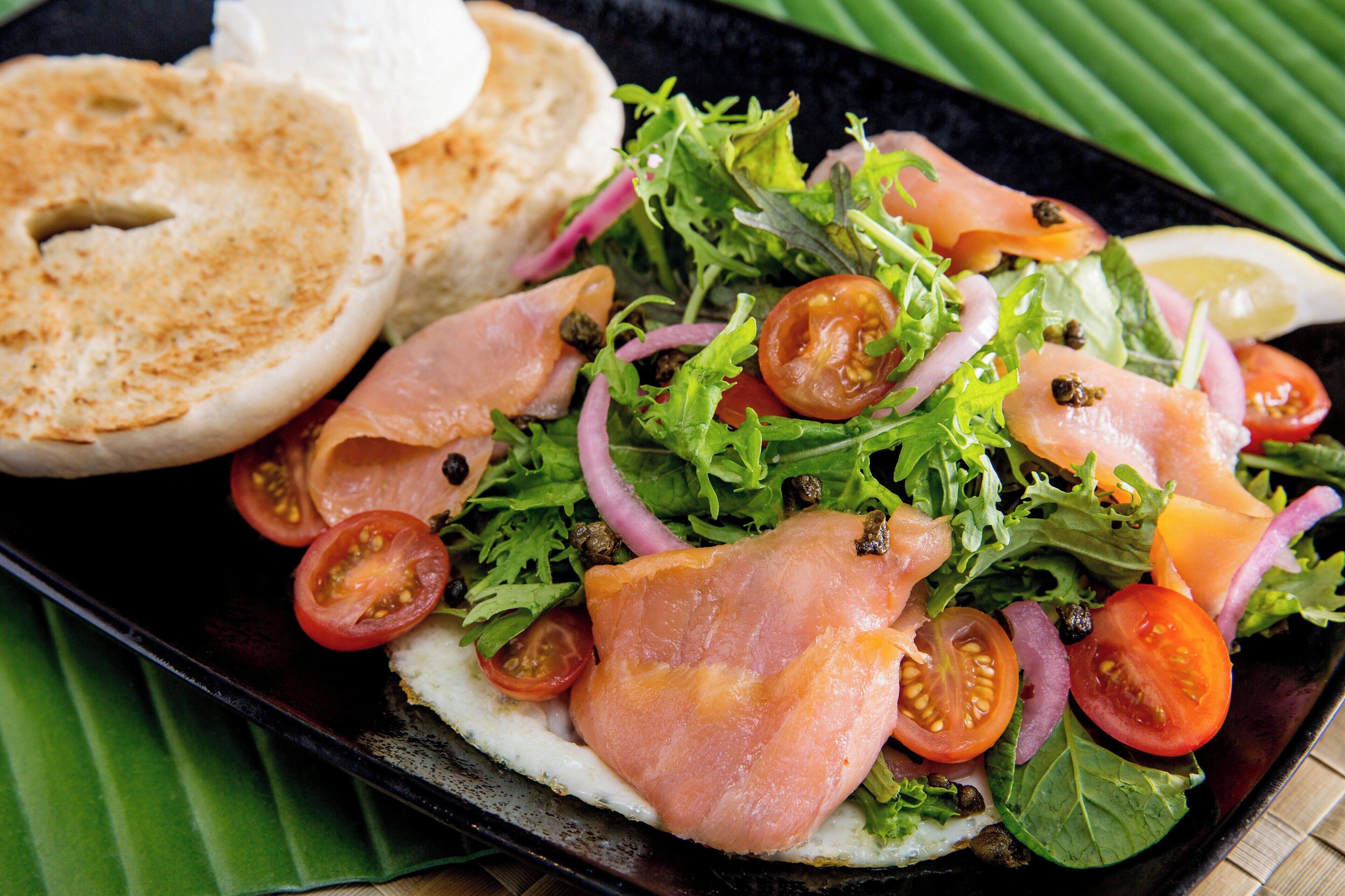 A plate of food with a salad, salmon, and a bagel.