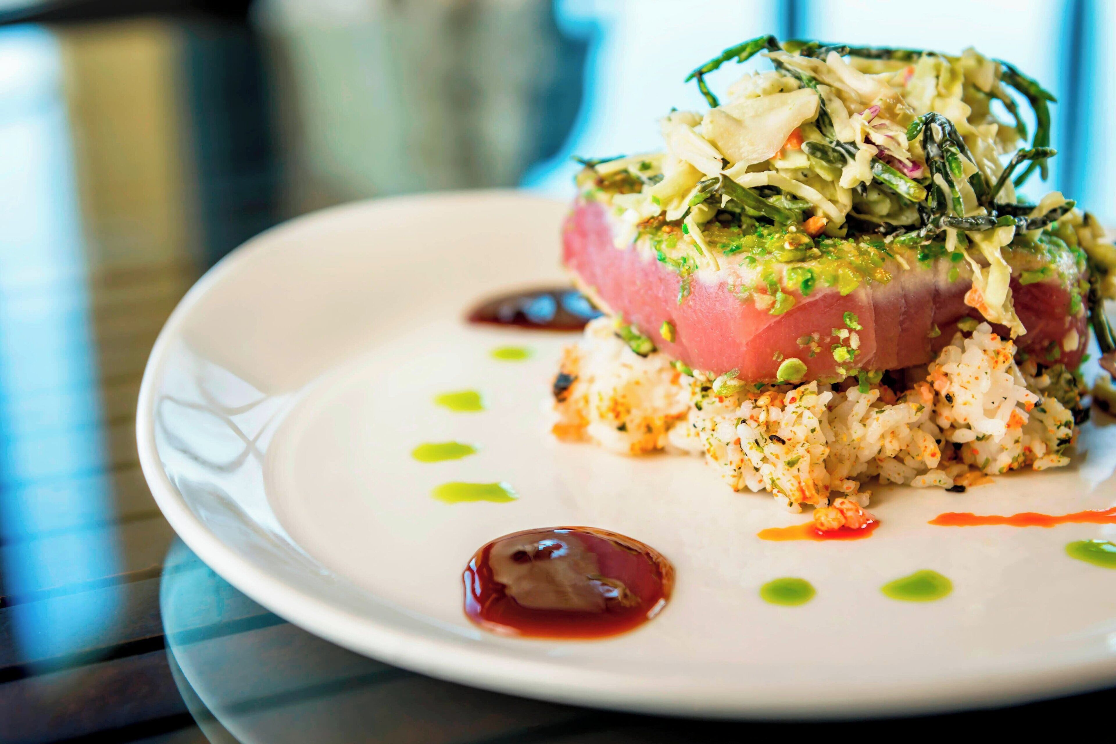 A plate of food with a variety of textures and colors, including a pinkish center, green toppings, and a base of grains or seeds.