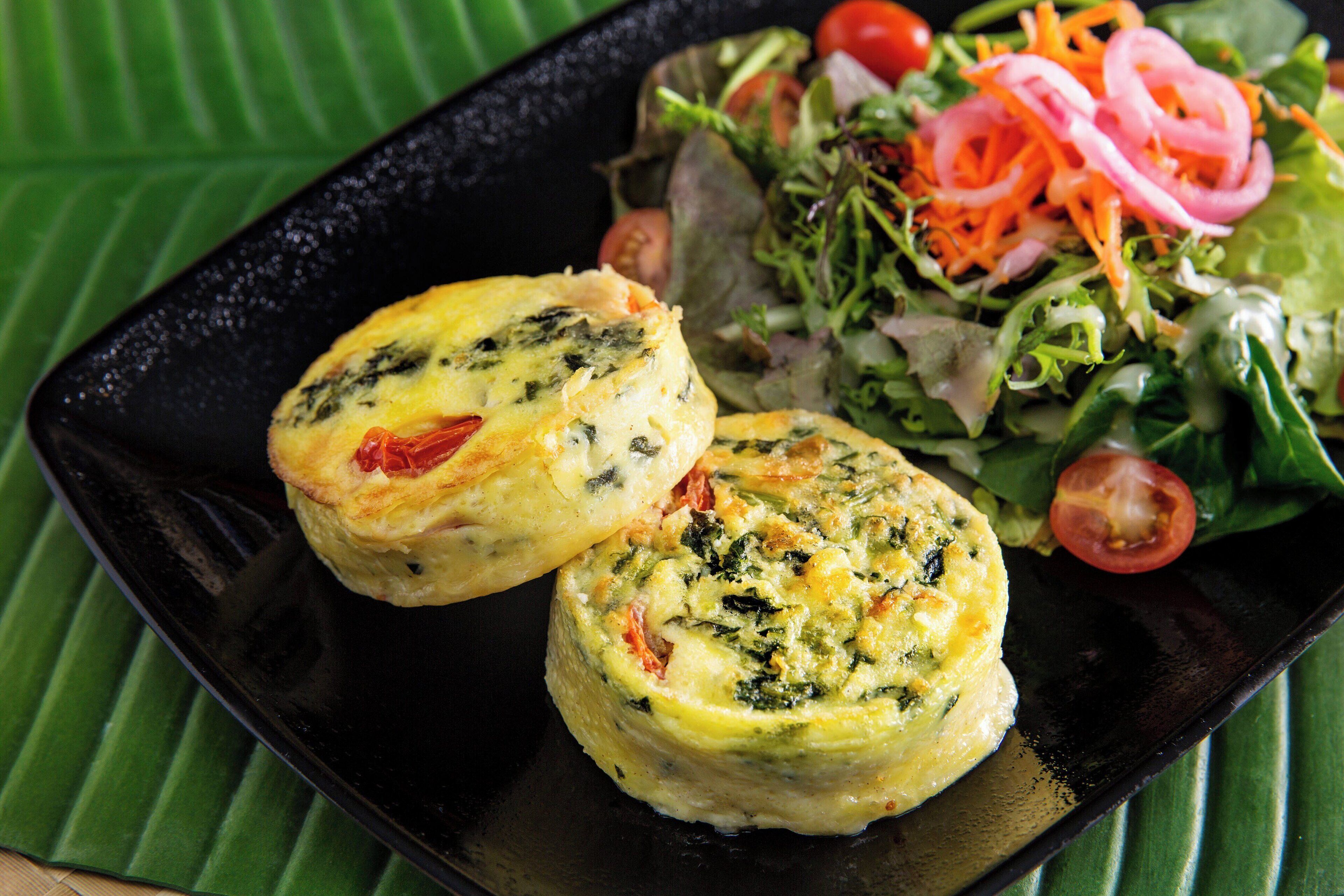 A black plate with two quiches and a salad with lettuce, tomatoes, and sliced onions.