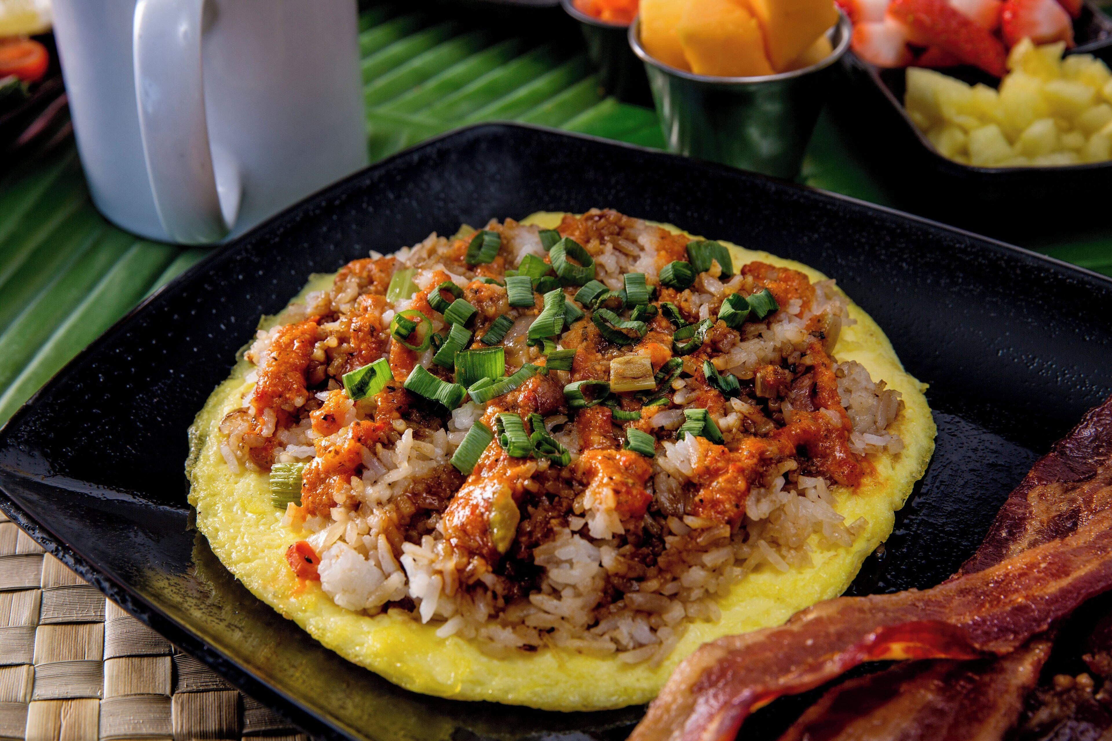 A breakfast dish with rice, eggs, and green onions on a black plate.