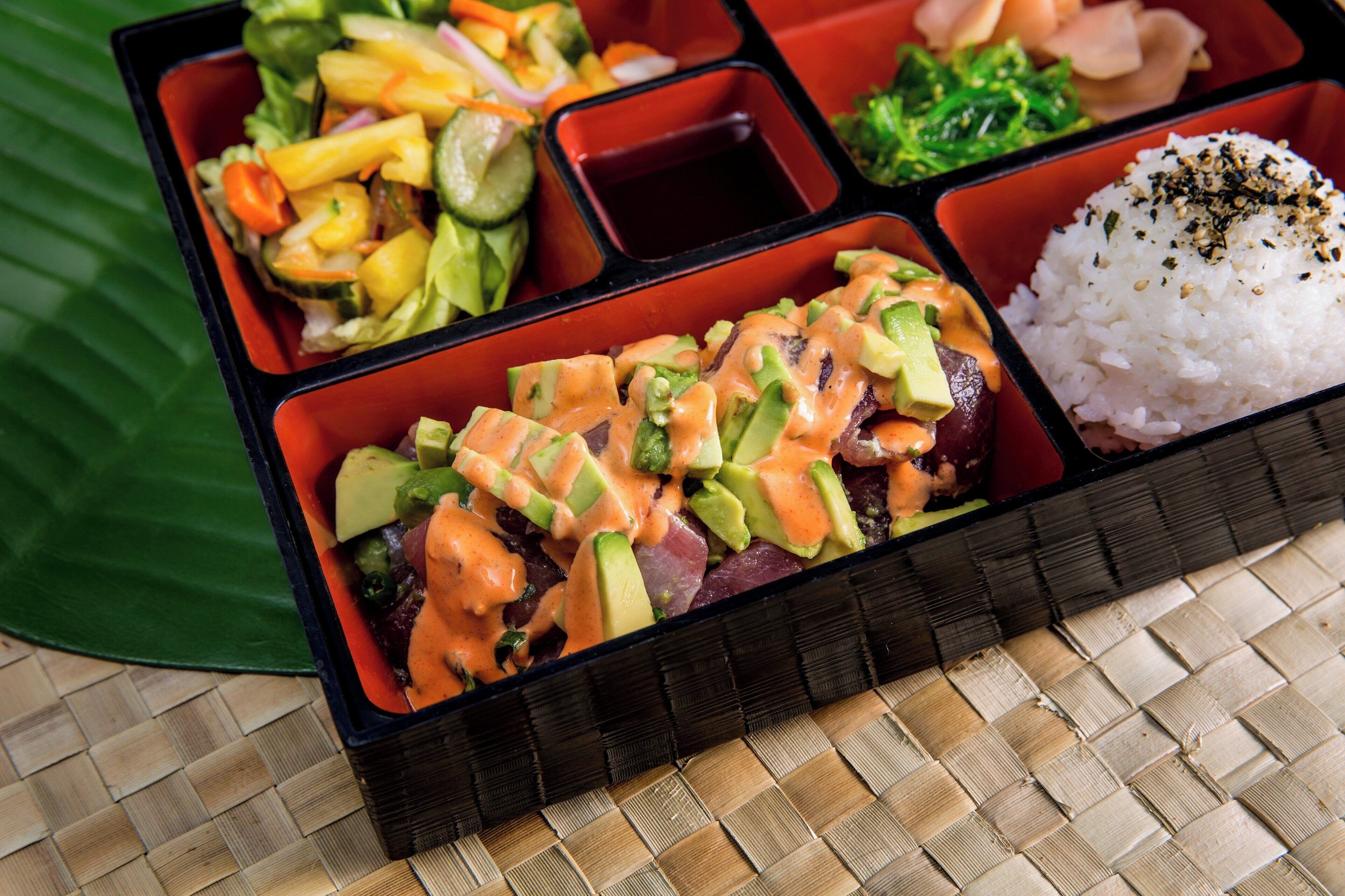 Una caja tipo bento con diversos alimentos, como arroz, verduras y un plato de carne, todo dispuesto ordenadamente en compartimentos.
