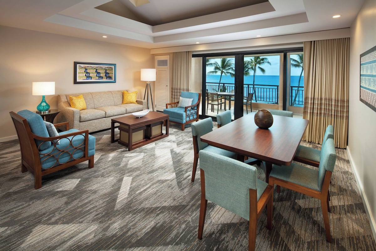 A hotel room with a balcony, a sofa, a dining table, and chairs.