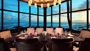 A dining area with a view of the ocean, large windows, and a chandelier. - Sheraton Kauai Resort (Koloa)