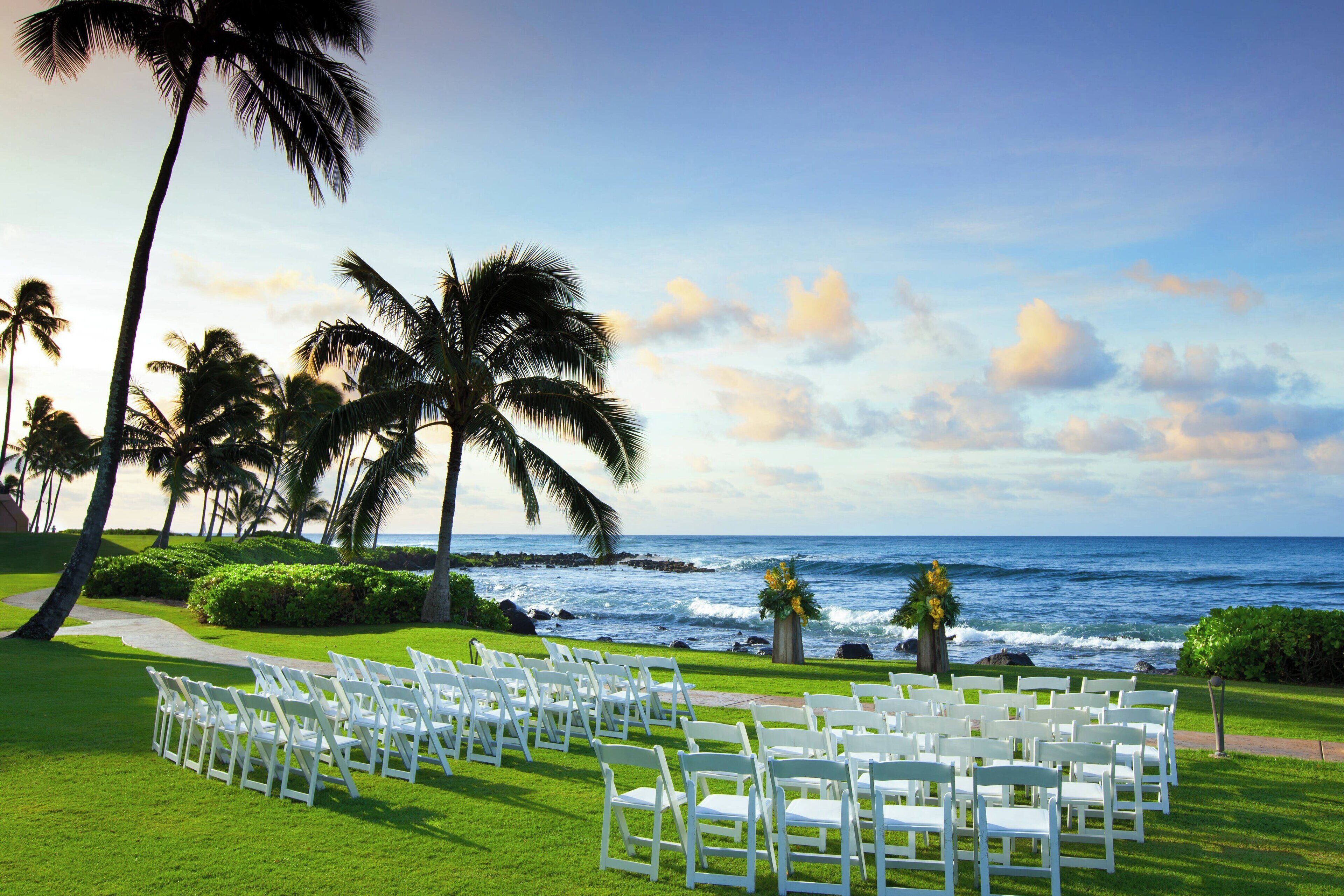 A wedding ceremony setup with white chairs arranged on a grassy lawn overlooking the ocean.