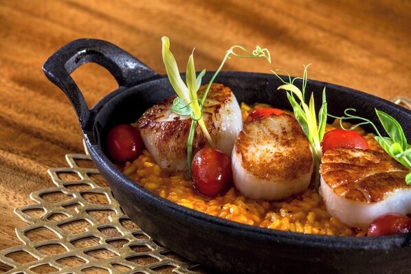 A skillet with seared scallops and cherry tomatoes on a wooden table. - Sheraton Kauai Resort (Koloa)