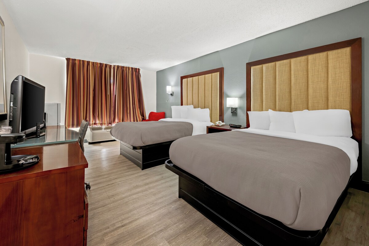 A hotel room with two beds, a TV, a desk, and a window with curtains.