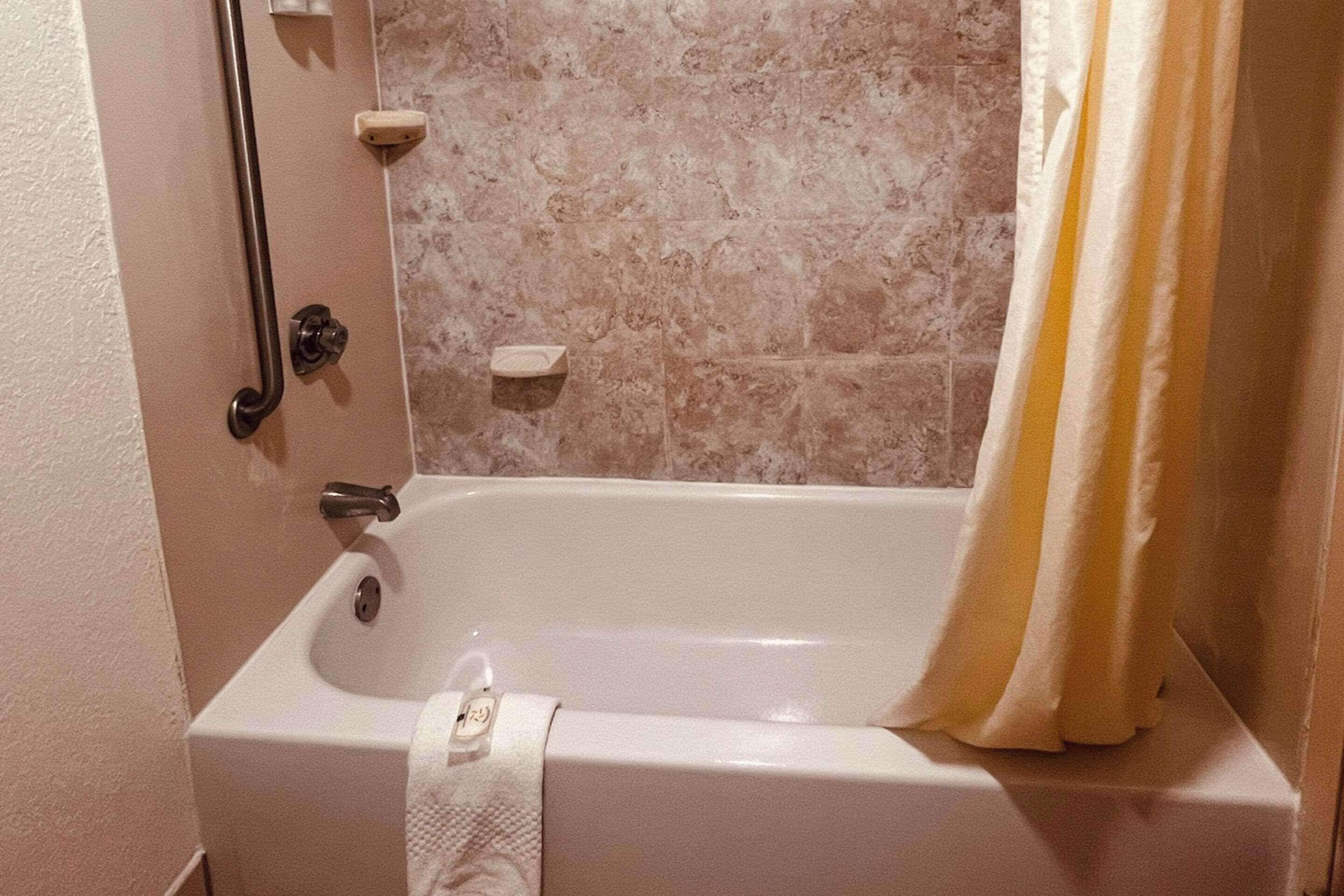 Et badeværelse med badekar, gelænder, håndklæde og væg i marmor.