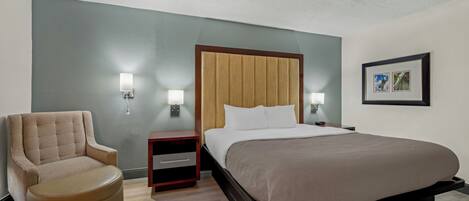 A hotel room with a bed, a chair, a nightstand, and a wall-mounted light fixture.
