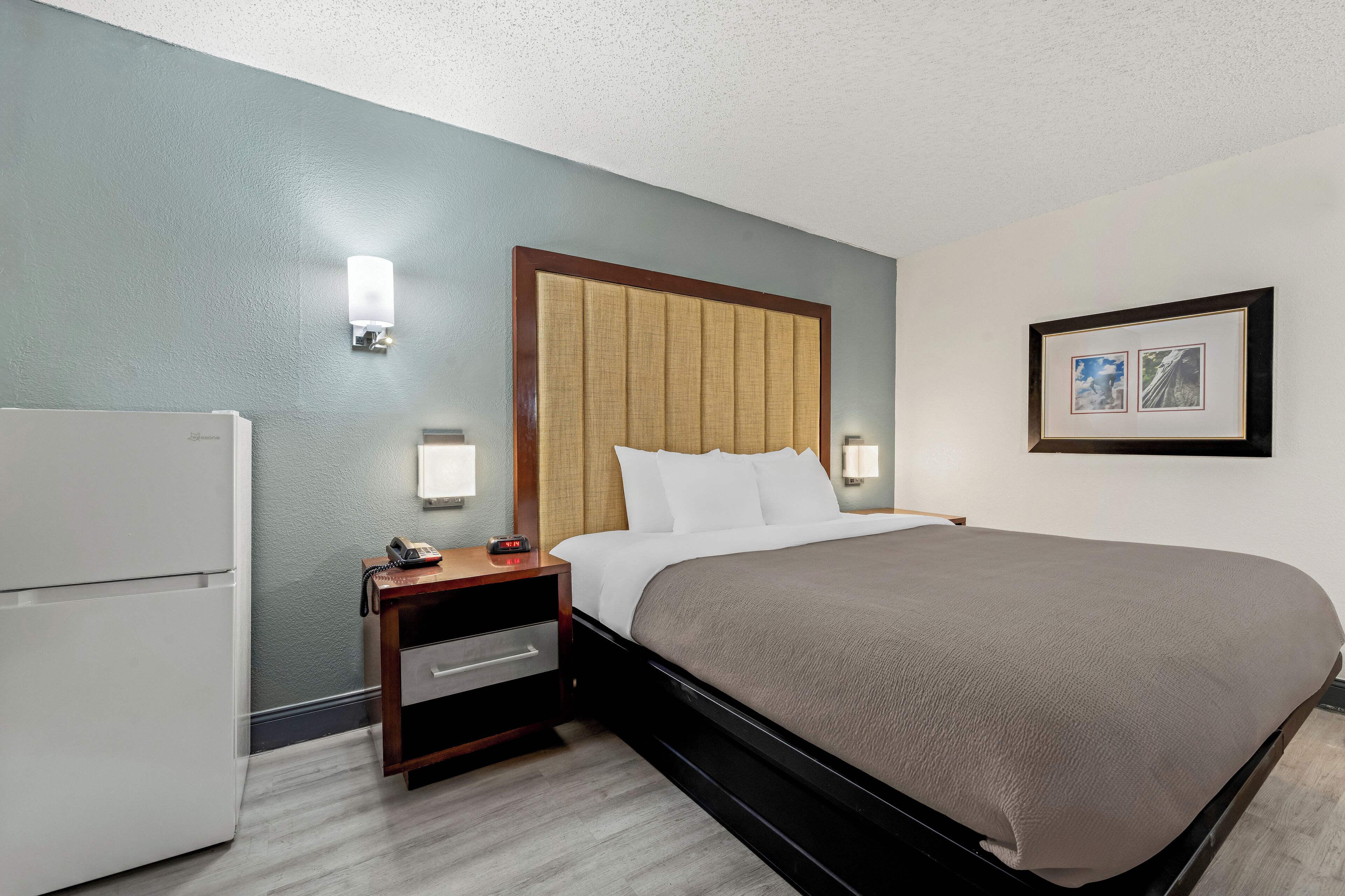 Habitación de hotel con cama, mesita de noche y refrigerador.